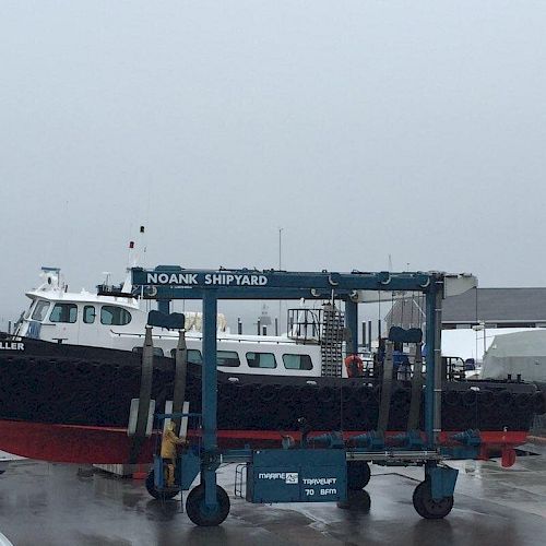 A ship named "Emil Miller" is being lifted by a large crane at Noank Shipyard on a foggy day, with other boats and buildings visible in the background.